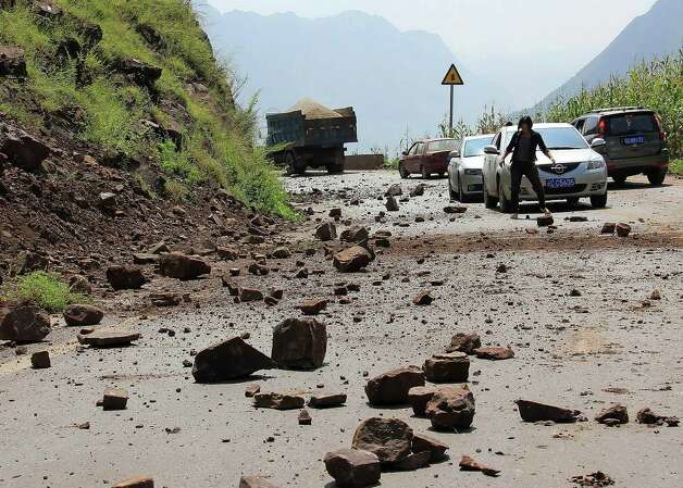 A woman tries to clear the fallen rocks from the mountain on a road near Zhaotong town, Yiliang County, southwest China's Yunnan Province, Friday. A series of earthquakes collapsed houses and triggered landslides Friday in a remote mountainous part of southwestern China where damage was preventing rescues and communications were disrupted. At least 64 deaths have been reported. (AP Photo) Photo: Associated Press / SL