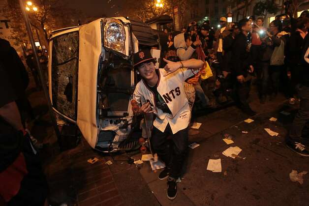 Leo Funaki stands in front of a car that was turned over on Market St. in San Francisco after the Giants won the World Series on Sunday, Oct. 28, 2012. Photo: Mathew Sumner, Special To The Chronicle / SF