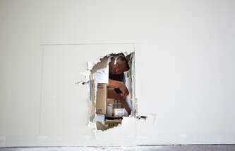 Don Hilliard looks through a hole burglars cut into the wall of Brashae's Beauty Supply.