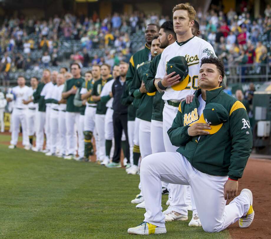 A’s catcher Bruce Maxwell takes a knee as outfielder Mark Canha puts his hand on his shoulder during the playing of the national anthem before a game against the Rangers at the Coliseum. Photo: Santiago Mejia, The Chronicle